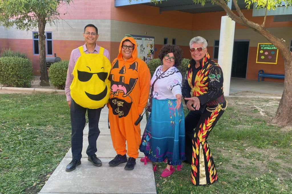 Two men and two women smile in their Halloween costumes outside the school