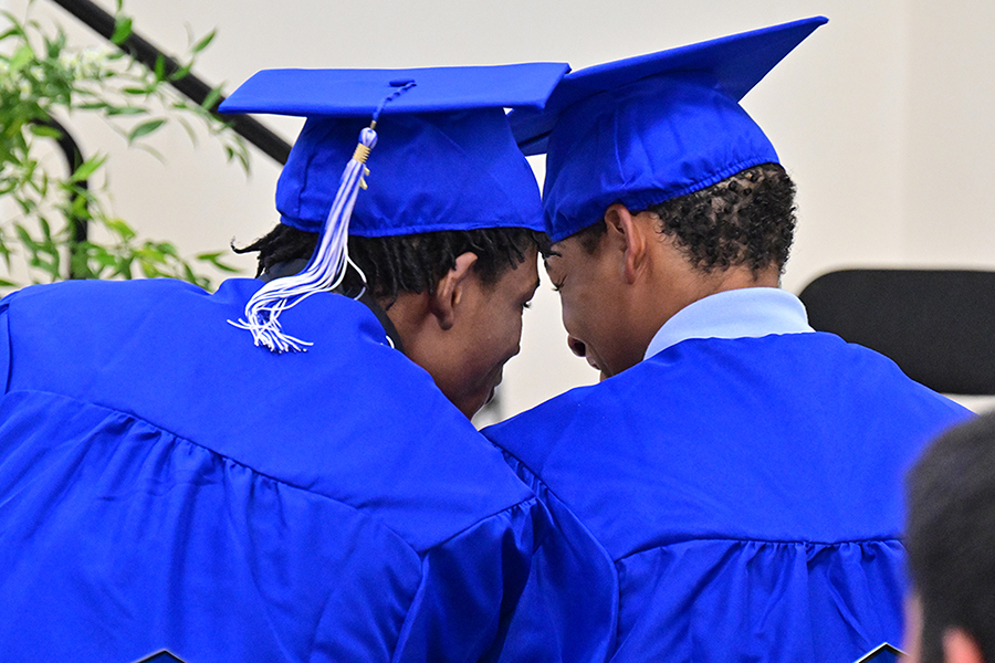 Two teen boys in their blue caps and gowns put their heads together during the ceremony