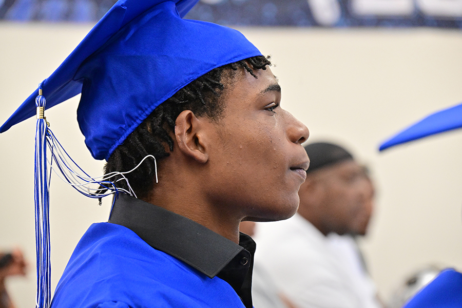 A teen boy in a blue cap and gown watches the ceremony intently