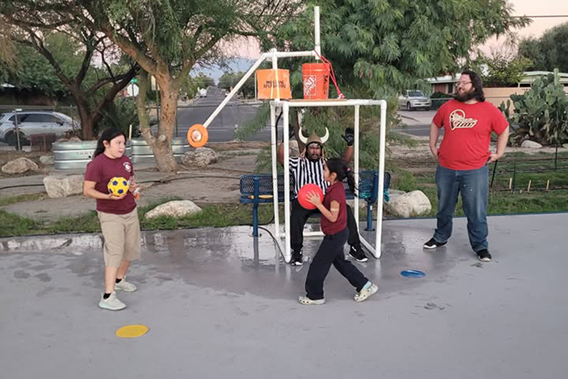 Two girls toss balls to dump water on a man in a black and white striped shirt and viking helmet