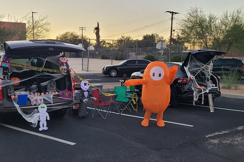 A kid dressed in an orange inflatable costume dances in front of a decorated trunk