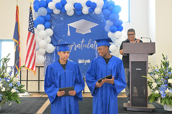 The two graduates stand in front of the stage, proudly holding their diplomas
