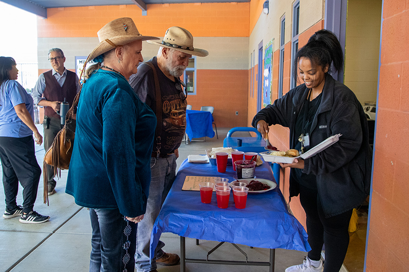 A woman serves up a Thanksgiving meal to a man and a woman in cowboy hats