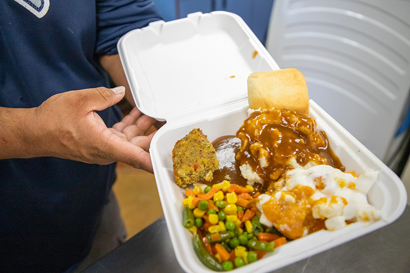 A man holds out his Thanksgiving meal in a takeout box