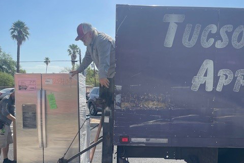 A man unloads a stainless steel fridge from a truck